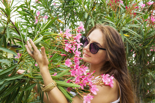Женщина нюхает олеандровые цветы в саду
 - Фото, изображение
