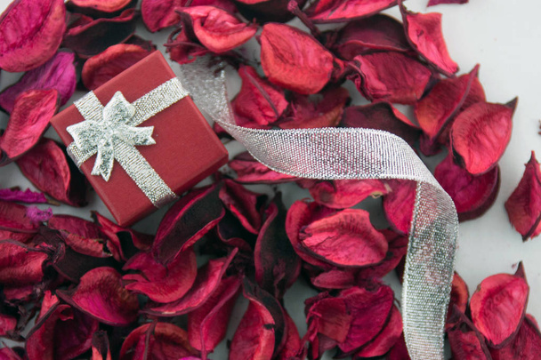Valentines day! Red box for a gift with silver ribbon and dry red petals, isolated on a white background. Top view. - Fotoğraf, Görsel