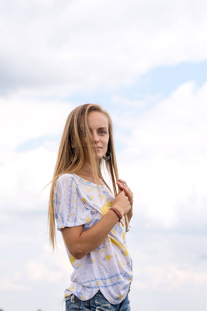 Long-haired young beautiful girl on a background of clouds - Photo, Image