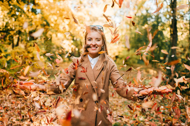 portrait of beautiful young woman in woollen coat with fallen leaves around - Фото, изображение