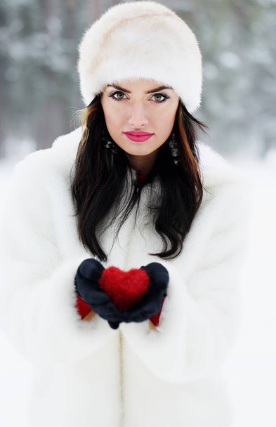Beautiful brunette in white winter clothes holding red heart. The concept of Valentine's Day - Photo, Image