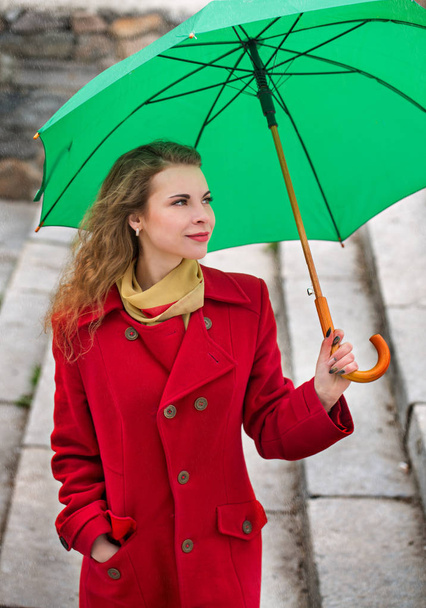 Mulher bonita em um casaco vermelho detém um guarda-chuva verde
 - Foto, Imagem