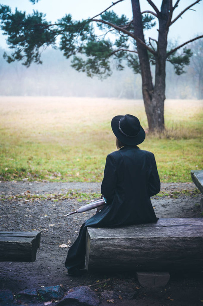 girl in a black coat sitting on a wooden bench - Photo, Image