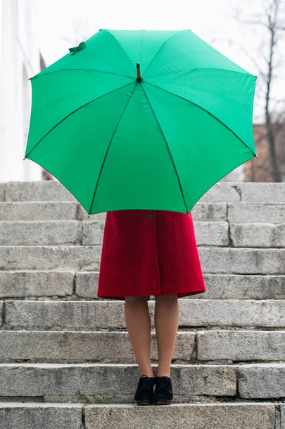 schöne Frau im roten Mantel hält einen grünen Regenschirm - Foto, Bild