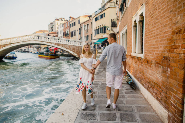 Young beautiful couple girl in dress man in white shirt walk through the streets of Venice Italy - Valokuva, kuva
