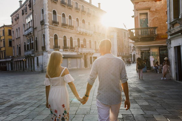 Young beautiful couple girl in dress man in white shirt walk through the streets of Venice Italy - Foto, Imagem