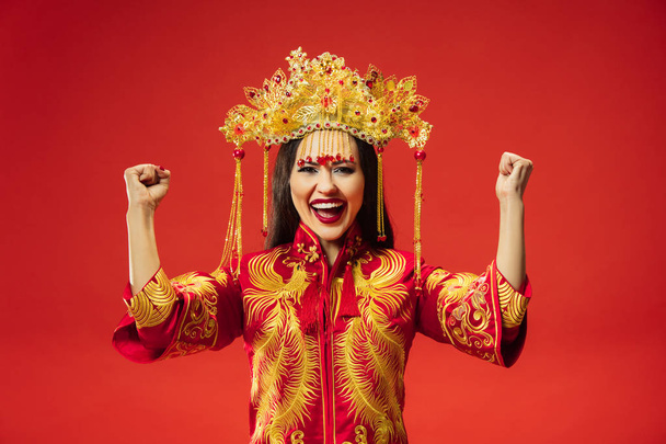 Chinese traditional graceful woman at studio over red background. Beautiful girl wearing national costume. Chinese New Year, elegance, grace, performer, performance, dance, actress, dress concept - Photo, Image