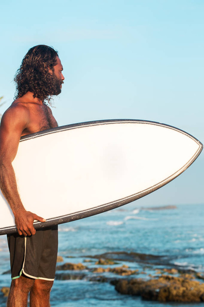 Le surfeur tient une planche de surf sur la côte de l'océan Indien
 - Photo, image