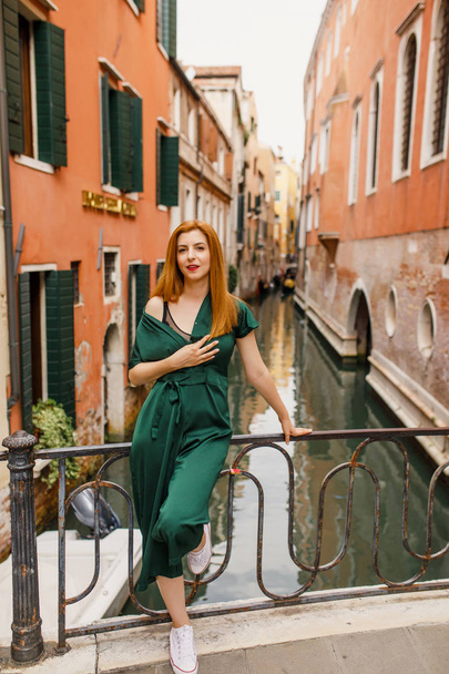 young beautiful girl with red hair and green dress is standing on the balcony in the beautiful city of Venice in Italy - Foto, immagini