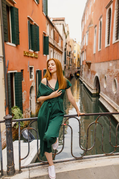 young beautiful girl with red hair and green dress is standing on the balcony in the beautiful city of Venice in Italy - Valokuva, kuva