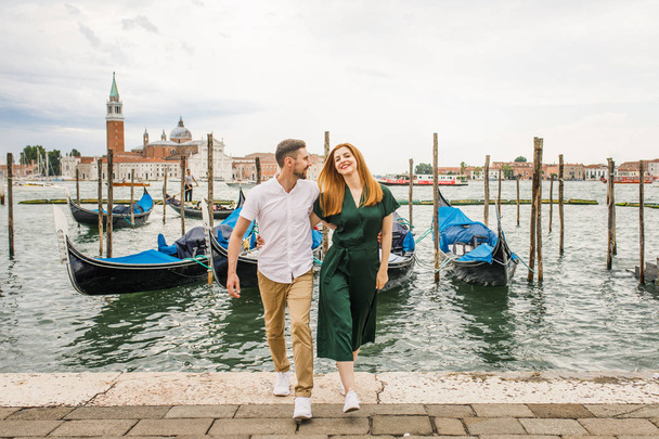 Young beautiful couple girl in a green dress a man in a white shirt walk near the water overlooking the Grand Canal in Venice Italy - Photo, image