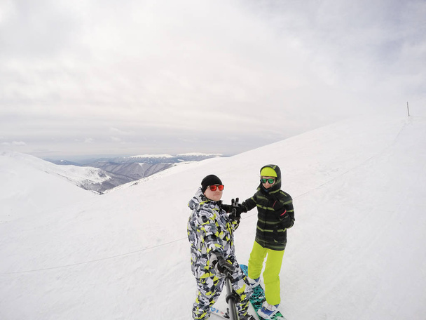 Dívka na snowboardu a chlapík na lyžích v horách. Spousta sněhu. Karpaty. Lyžařská bunda a kalhoty. Dvojice na aktivní zimní odpočinek - Fotografie, Obrázek