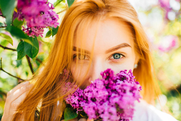 young attractive woman in park with blooming lilac bushes - Foto, Imagen