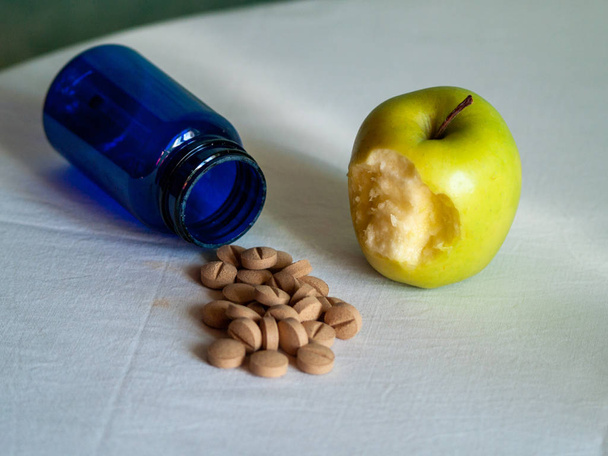 A bitten apple and a blue container with vegetable fiber pills on a table - Photo, Image