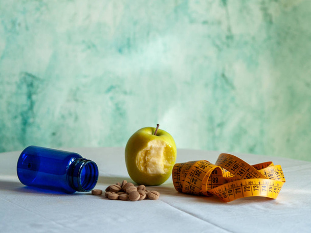 Una manzana mordida, una cinta métrica y un recipiente azul con píldoras de fibra vegetal sobre una mesa
 - Foto, Imagen