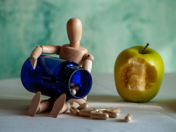 eine Holzfigur mit einem angebissenen Apfel und einem blauen Behälter mit Gemüsefasertabletten auf einem Tisch - Foto, Bild