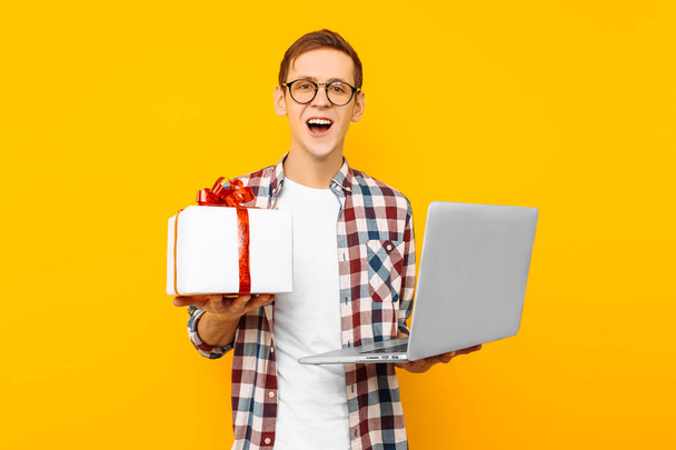 a man with a gift and a laptop in his hands, on a yellow background, online shopping, for Valentine's day - Zdjęcie, obraz