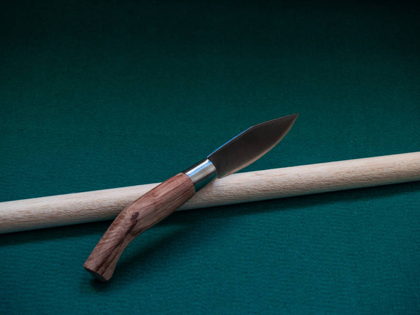 Un couteau pliant traditionnel avec la poignée en bois et un bâton en bois sur un tapis vert
 - Photo, image