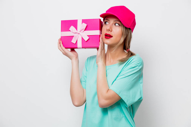 Belle jeune fille en bonnet rose et t-shirt bleu avec boîte cadeau de vacances sur fond blanc
. - Photo, image