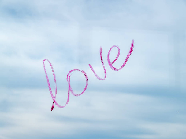 Έννοια της αγάπη τη λέξη αγάπη γράφεται με rouge κραγιόν σε ένα παράθυρο με το μπλε του ουρανού τα σύννεφα και - Φωτογραφία, εικόνα