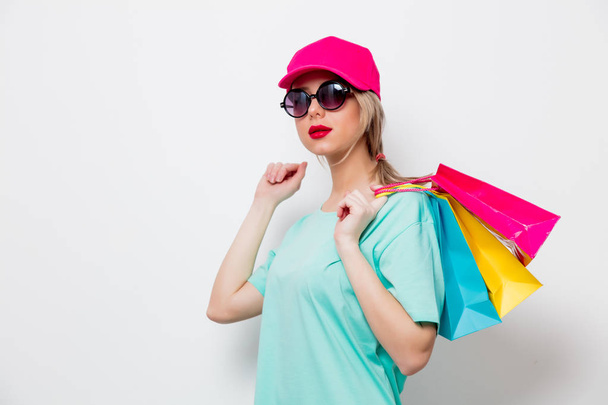 Beautiful young girl in pink cap and blue t-shirt with shopping bags on white background. - Fotografie, Obrázek