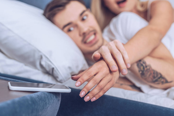 ritagliato colpo di uomo arrabbiato che tiene la mano della moglie che raggiunge per smartphone in camera da letto
 - Foto, immagini
