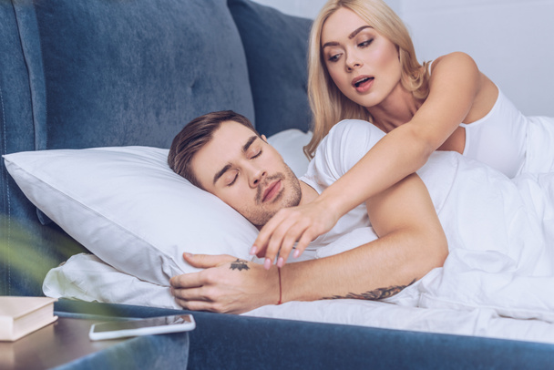 mujer celosa alcanzar para el teléfono inteligente mientras el novio duerme en la cama, concepto de desconfianza
   - Foto, imagen