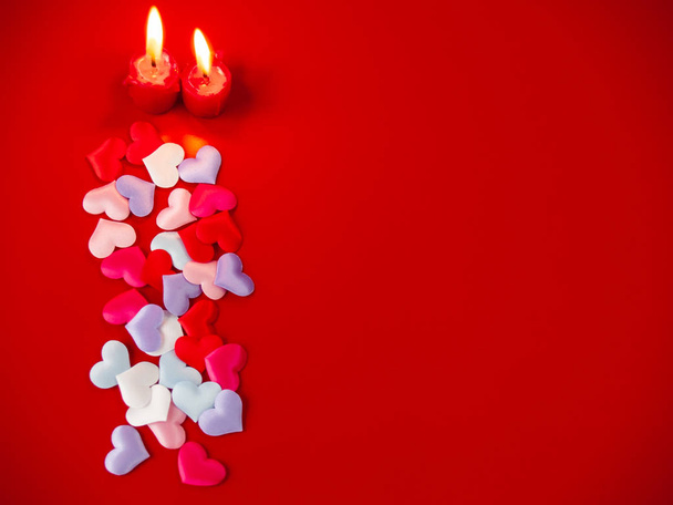 Concept of love Red candles lit and a lot of multicolor hearts with a red background - Photo, Image