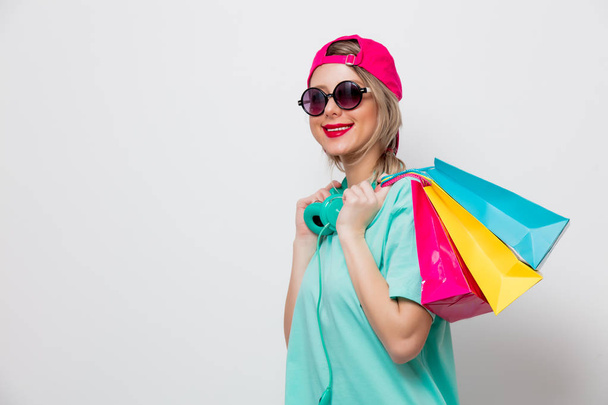 Hermosa joven en gorra rosa y camiseta azul con bolsas de compras sobre fondo blanco
. - Foto, imagen