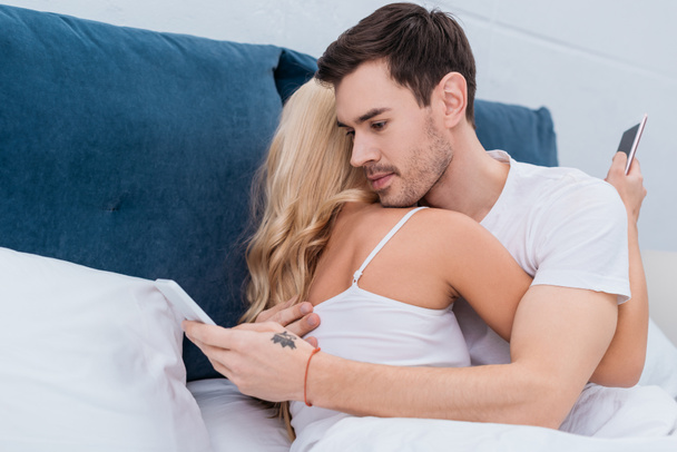 young couple hugging and using smartphones in bed, relationship problem concept  - Foto, Imagem