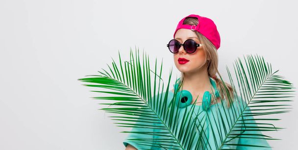 Beautiful young girl in pink cap and blue t-shirt with green palm branch on white background. - Valokuva, kuva