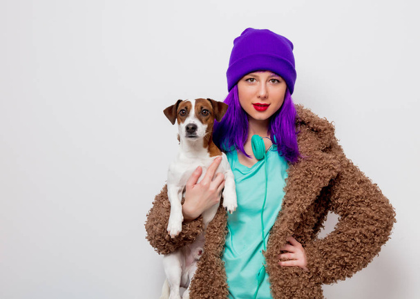 Красивая молодая девушка с фиолетовыми волосами в куртке держа собаку на белом фоне
. - Фото, изображение