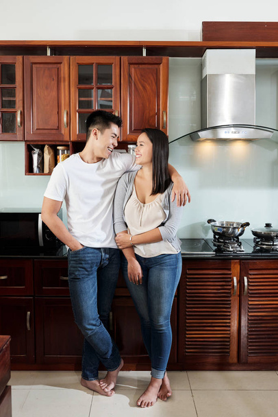 Happy Asian boyfriend and girlfriend hugging and looking at each other in new apartment - Photo, Image