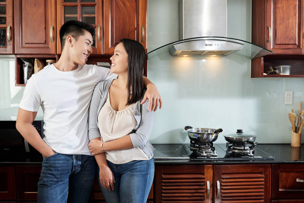 Young happy couple in love standing in kitchen and looking at each other - Fotó, kép