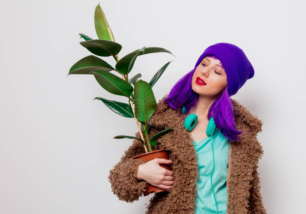 Mooi jong meisje met paars haar in jas met plant op witte achtergrond. - Foto, afbeelding