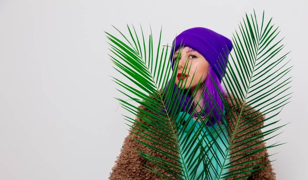 白い背景の上のヤシの葉のジャケットに紫の髪の美しい少女. - 写真・画像