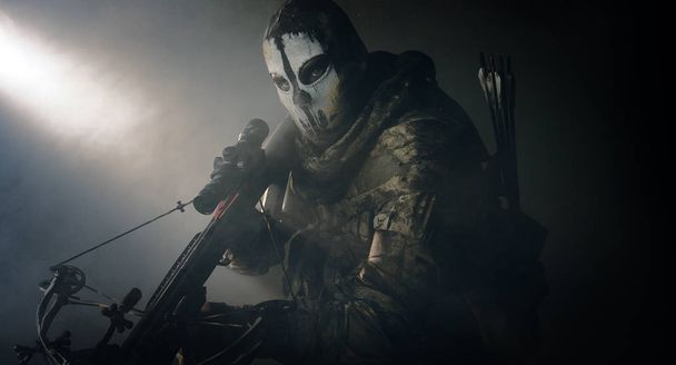 warrior man in mask with crossbow posing against cold grey background - Фото, зображення
