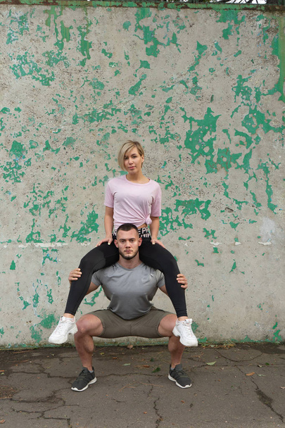 Muscular man is squatting during the workout with the girl on his shoulders - Fotó, kép
