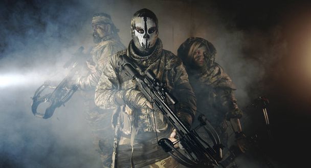 group of hunters in camouflage with modern weapons posing in dark building - Foto, Imagem