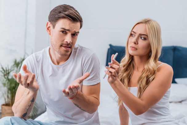 upset woman showing smartphone to emotional suspicious husband sitting on bed - Fotoğraf, Görsel