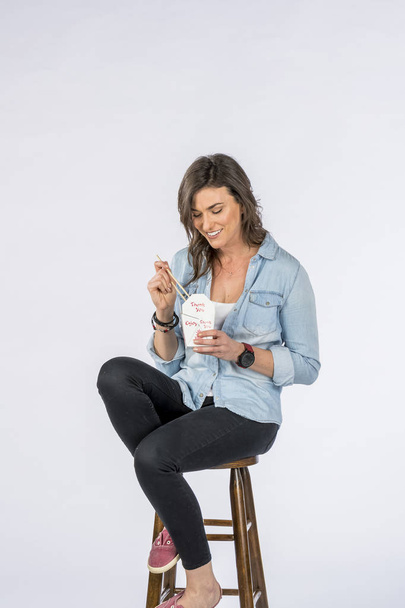 Gorgeous long haired brunette model eating chinese food against  white background in a studio environment - Photo, image