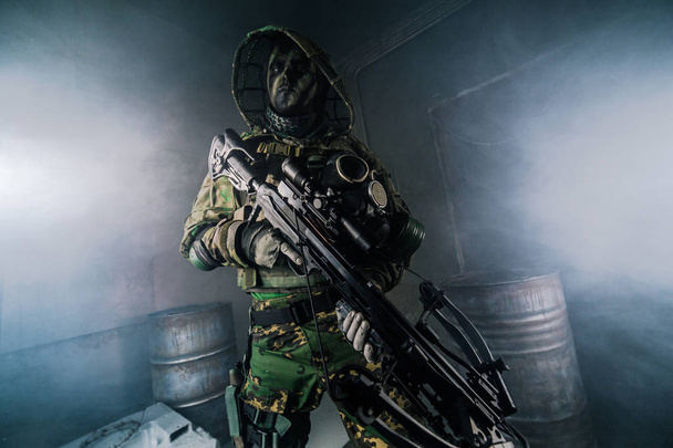 hunter man in camouflage with crossbow posing against dark background - Valokuva, kuva