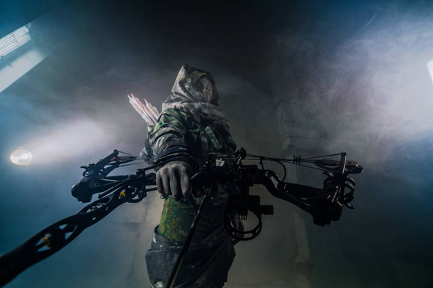 hunter woman in camouflage with bow posing in dark building indoors - Photo, Image