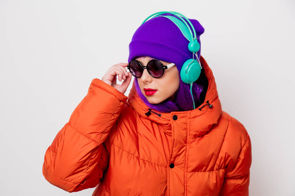 Krásná mladá dívka s fialovými vlasy a oranžová bunda poslouchat hudbu ve sluchátkách na bílém pozadí. - Fotografie, Obrázek