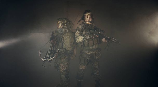 δύο άνδρες κυνηγών στο καμουφλάζ με βαλλίστρα θέτοντας σε σκούρο φόντο - Φωτογραφία, εικόνα