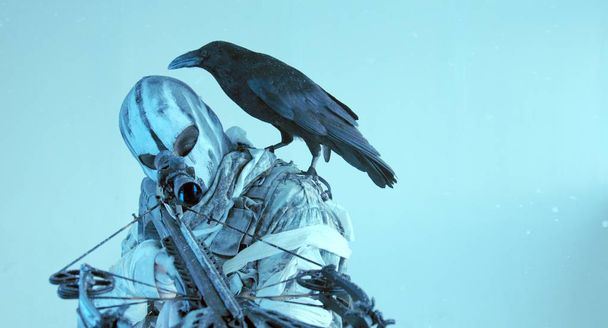 hunter in mask with modern crossbow and raven posing against cold blue background - Foto, afbeelding