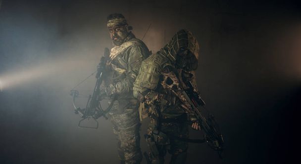 two male hunters in camouflage with crossbows posing against dark background - Valokuva, kuva