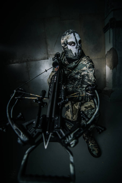 warrior man in mask with crossbow posing against cold grey background - Photo, Image