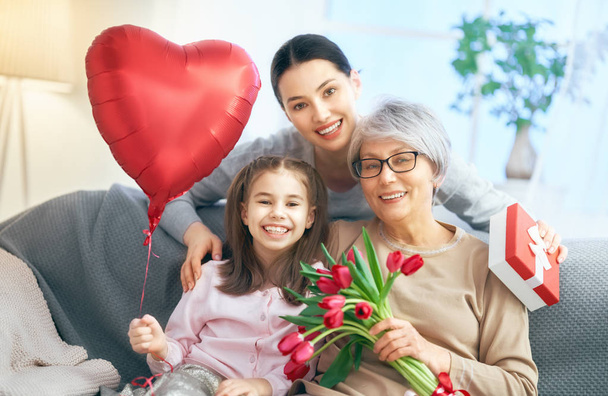 Happy women's day! Child daughter is congratulating mom and granny giving them flowers tulips. Grandma, mum and girl smiling and hugging. Family holiday and togetherness. - Фото, зображення