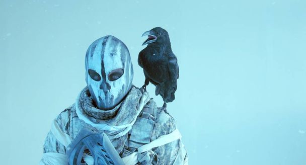 closeup view of hunter in mask with raven posing against cold blue background - Photo, image